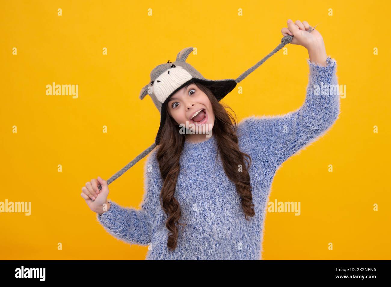 Fashion happy young woman in knitted hat and sweater having fun over colorful blue background. Excited teenager girl. Stock Photo