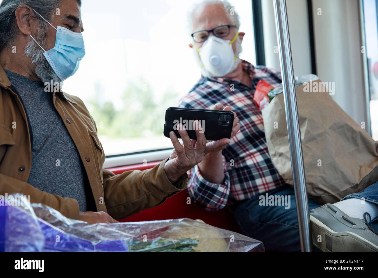 Senior male passengers in face masks using smart phone on subway Stock Photo