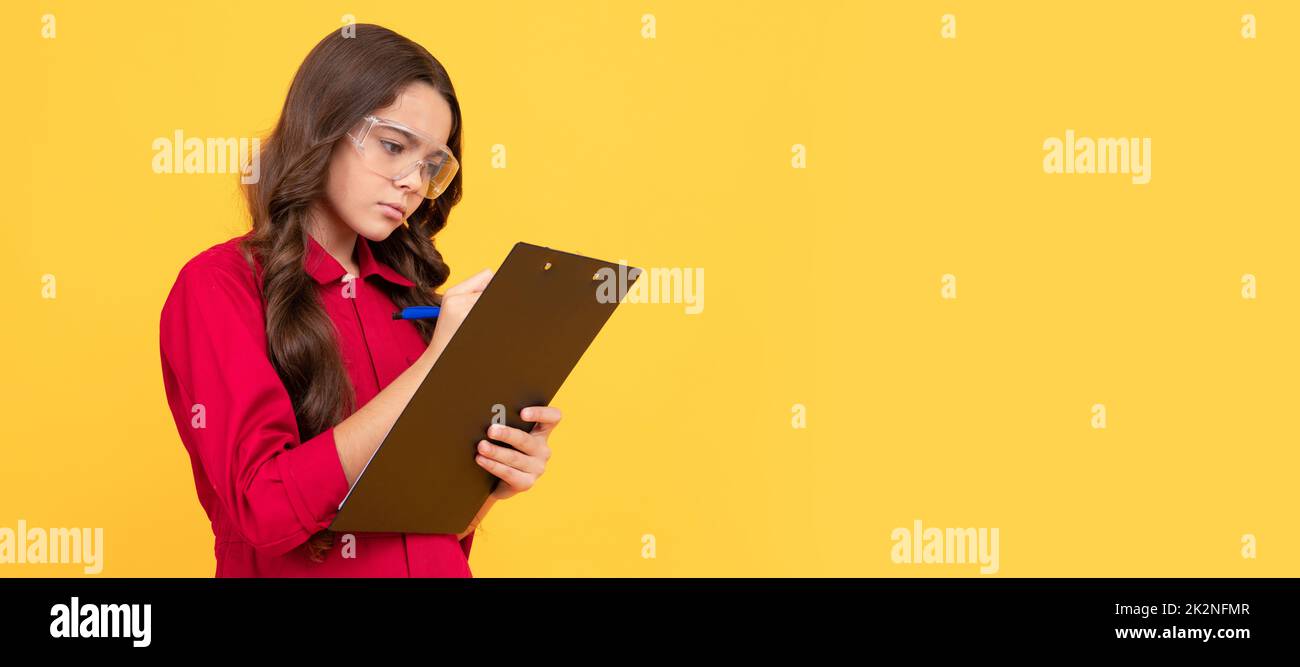 concentrated teenager girl in protective glasses making notes in folder with documents. Child builder with protective glasses horizontal poster design Stock Photo