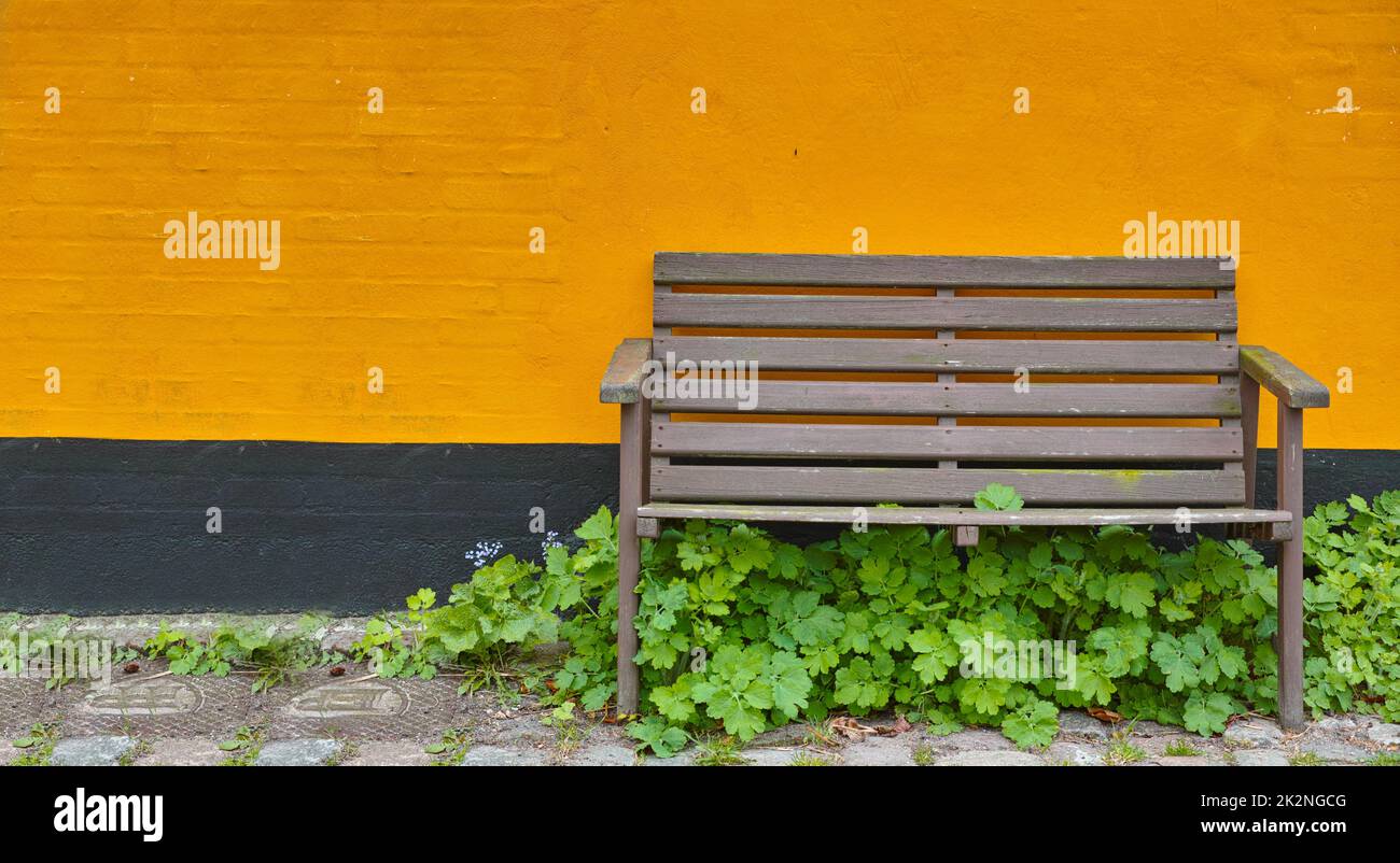 Take a seat.... A single wooden bench against a bright orange wall. Stock Photo