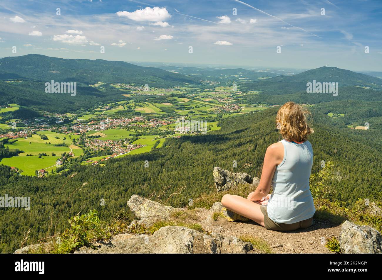 A woman sitting on mount Osser, overlooking the landscape of Lamer Winkel with the small town Lam in the Bavarian Forest Stock Photo