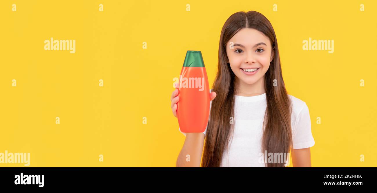 cheerful kid hold hair conditioner bottle and grapefruit on yellow background. Banner of child girl hair care, studio poster header with copy space. Stock Photo