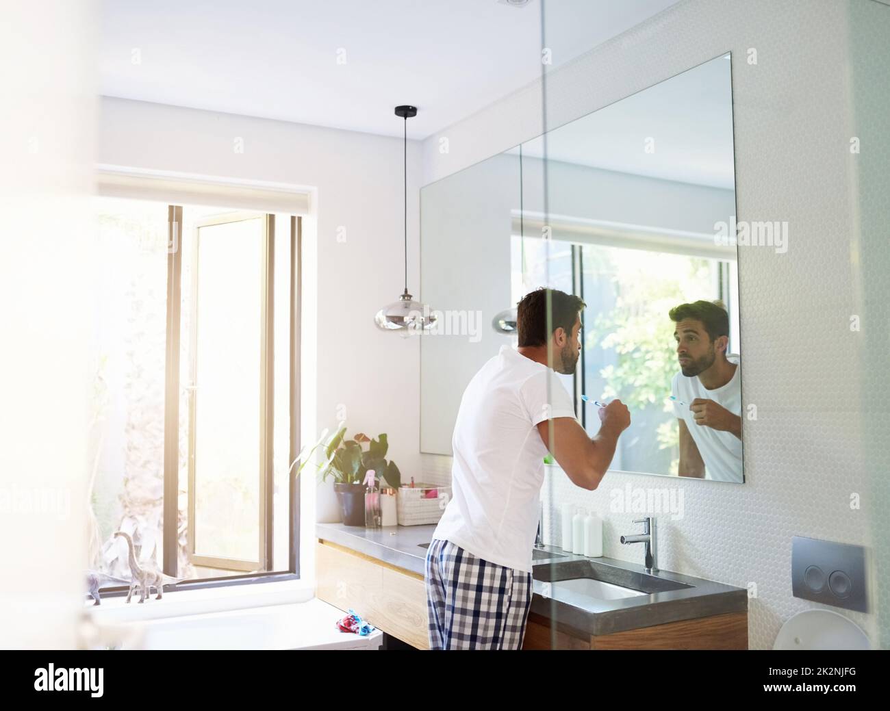 Twice a day keeps the dentist away. Cropped shot of a handsome man looking in the mirror and rinsing his mouth in the bathroom at home. Stock Photo