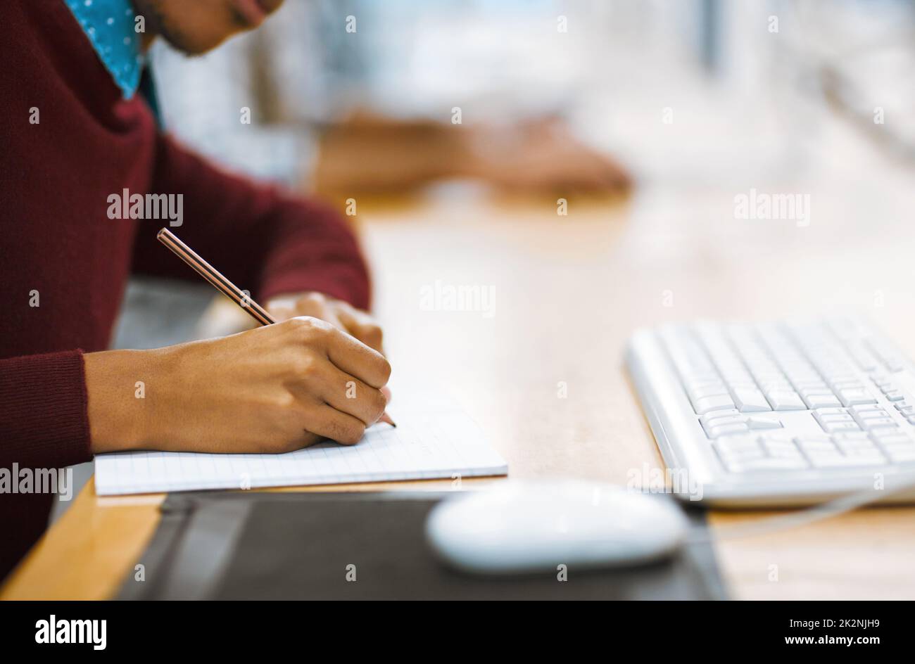 Always make notes when studying. Shot of a unrecognizable student writing down notes while working on a computer in a library. Stock Photo