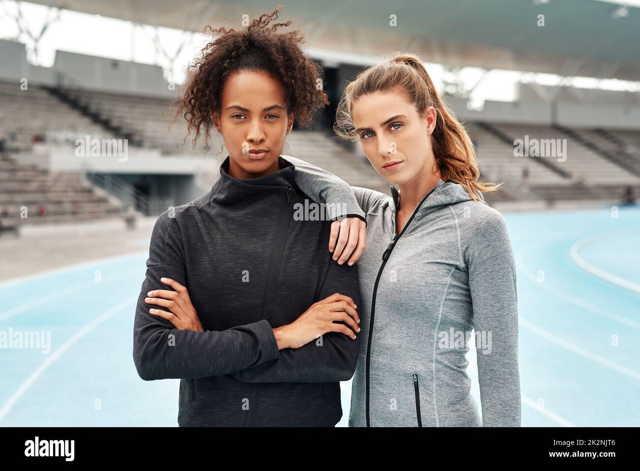 We dare you to try stop us. Cropped portrait of two attractive young athletes standing together after a run on a track field during a training session. Stock Photo