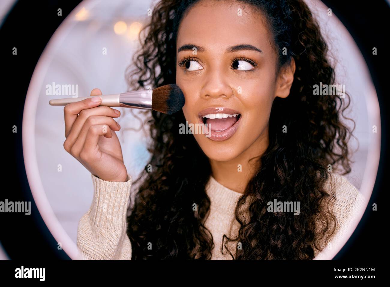 Tell me what you think about this look in the comments. Shot of a young woman doing her makeup while recording a video for her blog. Stock Photo