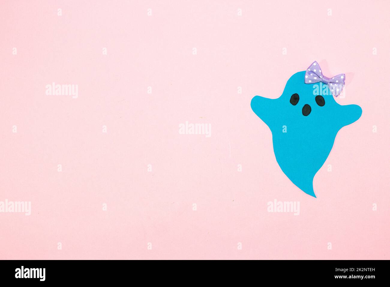 blue ghost with bow on right side pink background, copy space, creative halloween concept, flat lay, paper craft Stock Photo