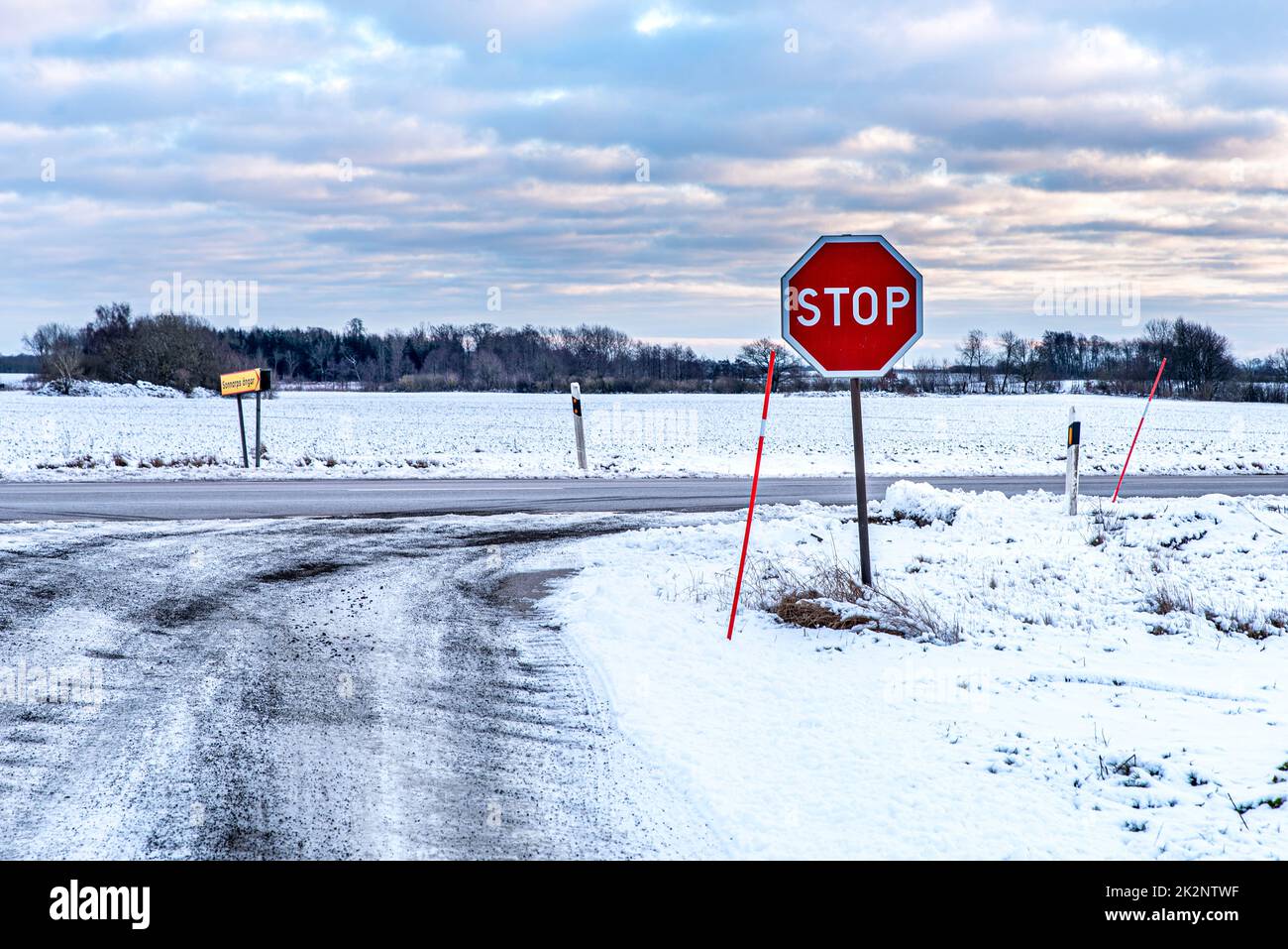 Frozen road in Swedish countryside with a stop sign. Nordic road covered by snow. Clouds and ice convey sense of desolation. Melancholy concept Stock Photo