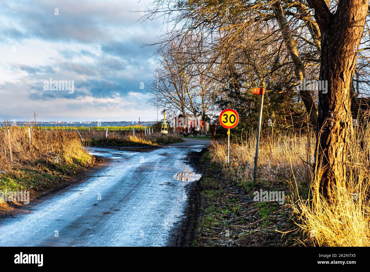 Countryside narrow road by the sea after a winter rain fall. Gloomy sky reflecting in a puddle conveys a sense of melancholy, solitude and loneliness Stock Photo