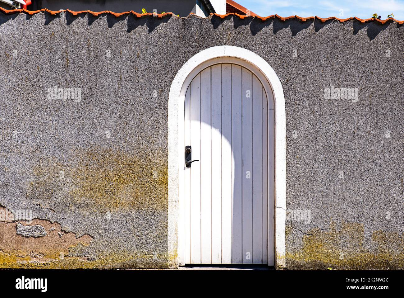 Front view of white arched closed door on worn grey wall conveys end of conversation or stop negotiation. Entrance or exit arch with shut wooden gate Stock Photo