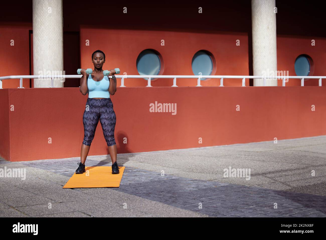 Your core/ your breath/your anchor. Shot of a young woman using dummbells on a gym mat against an urban background. Stock Photo