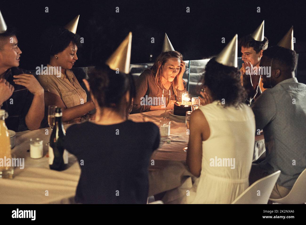 We hope all her wishes come true. Shot of a beautiful young woman blowing the candles on her birthday cake at a evening gathering with friends. Stock Photo