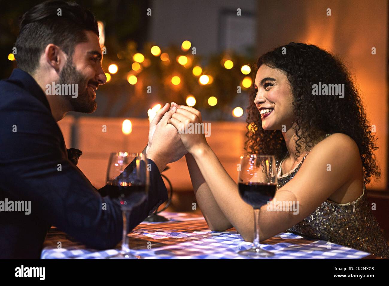 We will stay together forever. Shot of a cheerful young couple holding hands while looking into each others eyes over a candle lit dinner date at night. Stock Photo