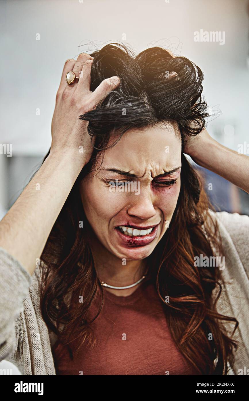 Shes cant take it anymore. Shot of a beaten and bruised young woman crying with her hands in her hair. Stock Photo