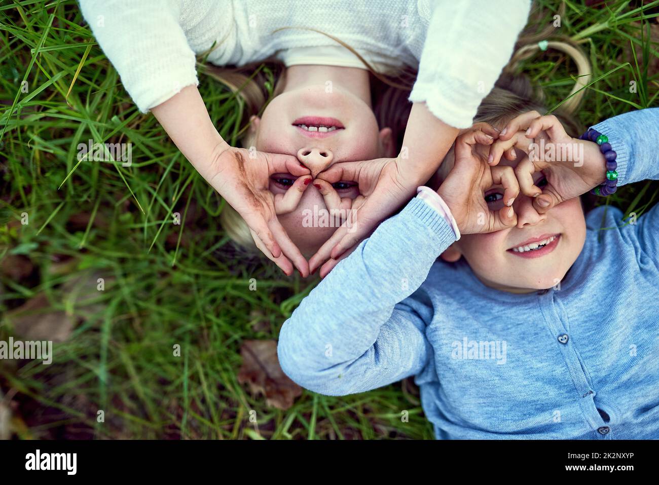 Being young is all about having non-stop fun. Portrait of two little sisters lying on the grass outside. Stock Photo