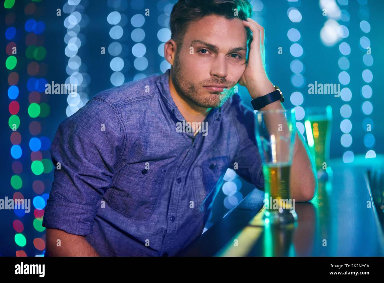 Here to drink all my sorrows away. Portrait of a young man looking upset while sitting at the bar in a club. Stock Photo