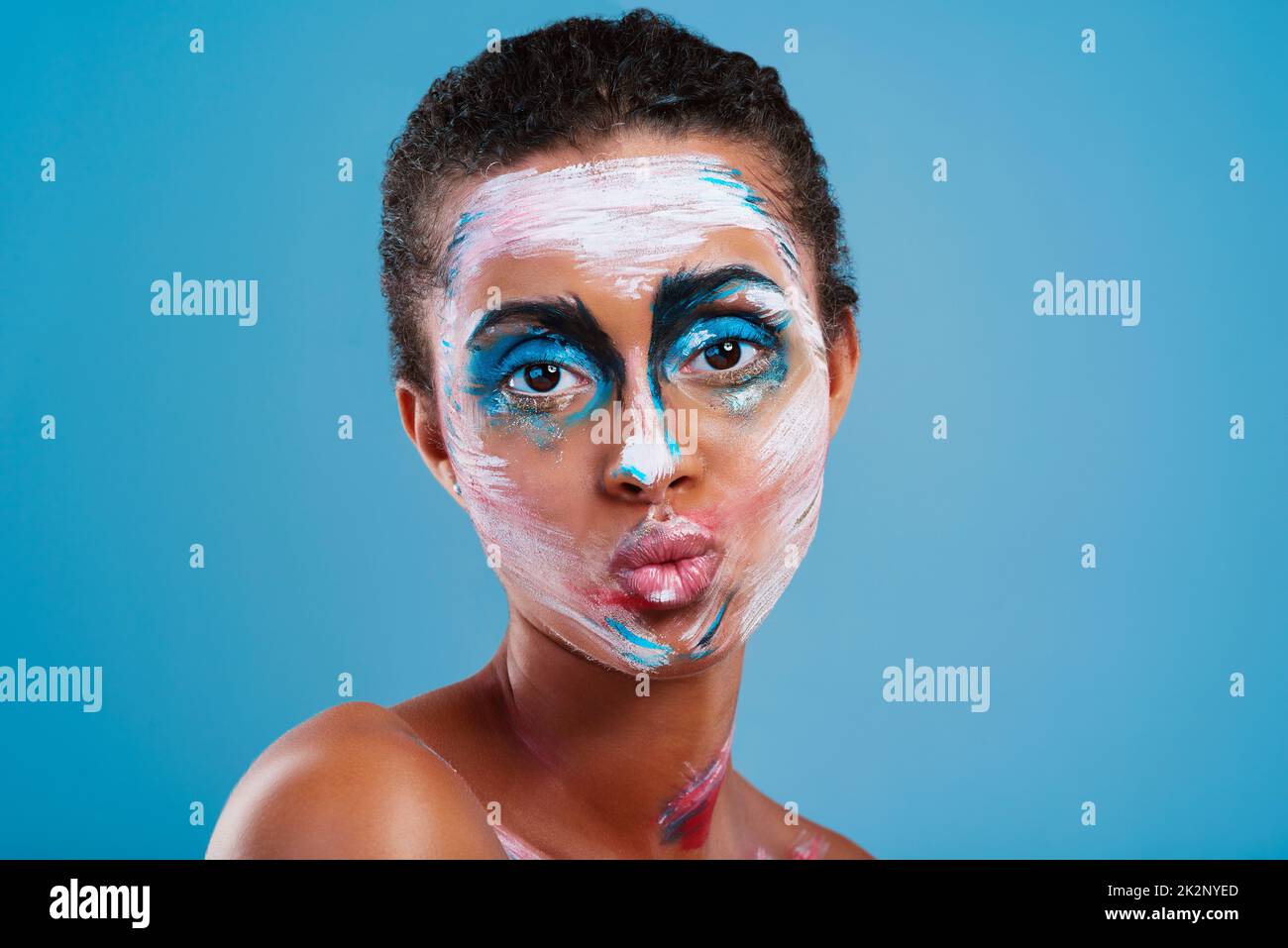 More than just a pretty face. Studio portrait of a beautiful young woman covered in face paint posing against a blue background. Stock Photo