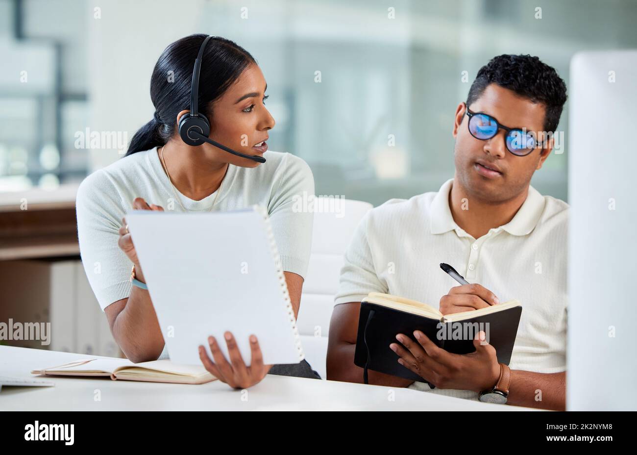 Are you making notes of these. Shot of an attractive young agent sitting with her trainee in the office and explaining while he writes notes. Stock Photo