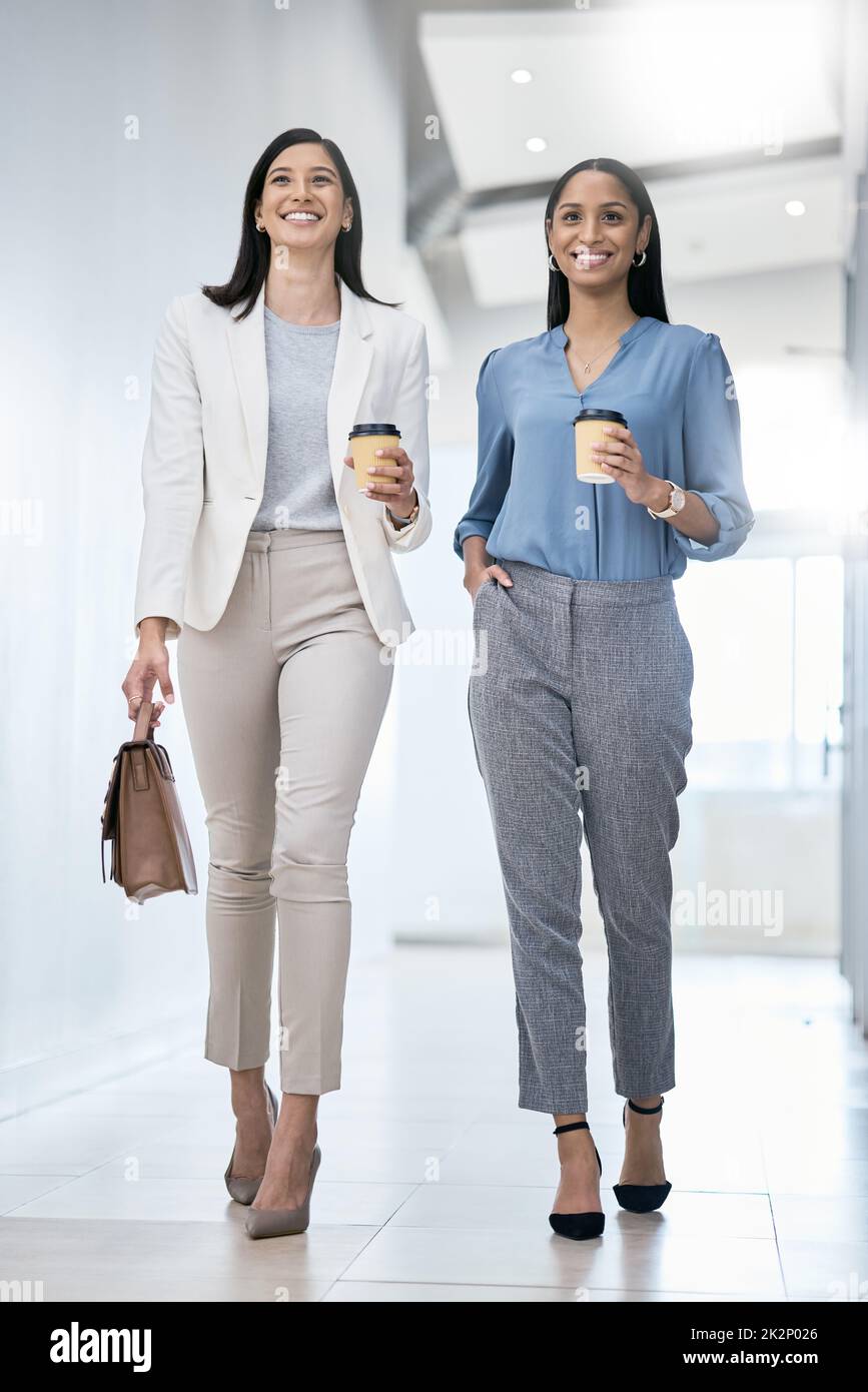 Lets go run this day. Shot of two businesswomen carrying coffees while walking through an office. Stock Photo