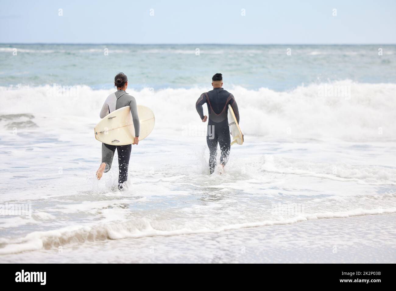 We belong in the ocean. Shot of an unrecognizable couple running into the water with surfboards at the beach. Stock Photo