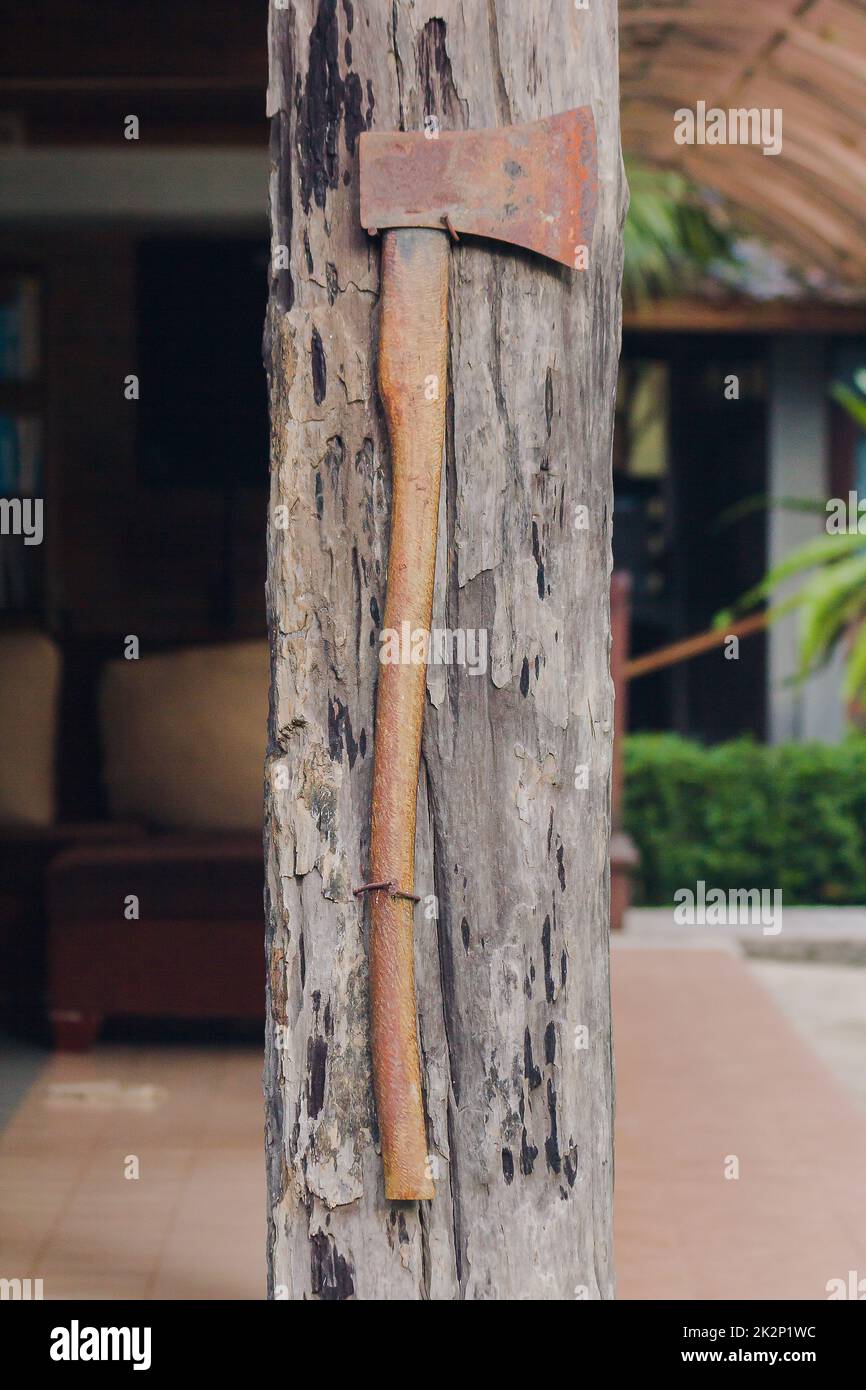 The old iron ax is attached to the wooden house pole. Stock Photo