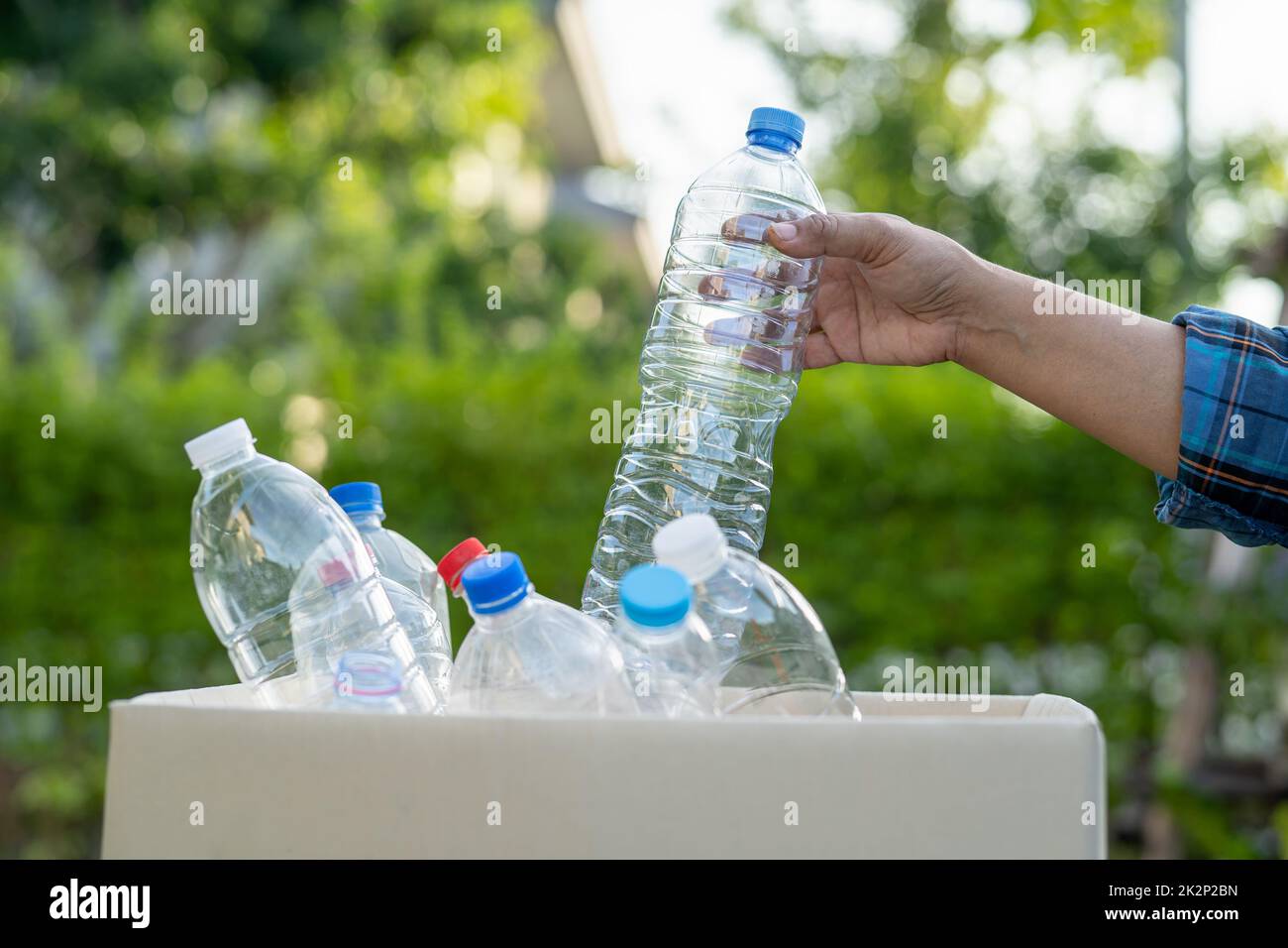 Asian woman volunteer carry water plastic bottles into garbage box trash in park, recycle waste