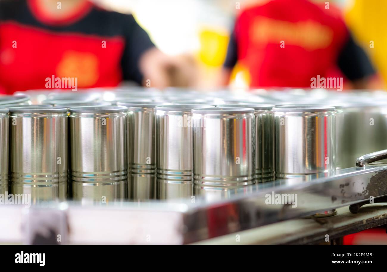 Many cans on blur workers. Canned fish factory. Food industry. Workers working in canned food factories to fill sardines in tinned cans. Food processing production line. Food manufacturing industry. Stock Photo