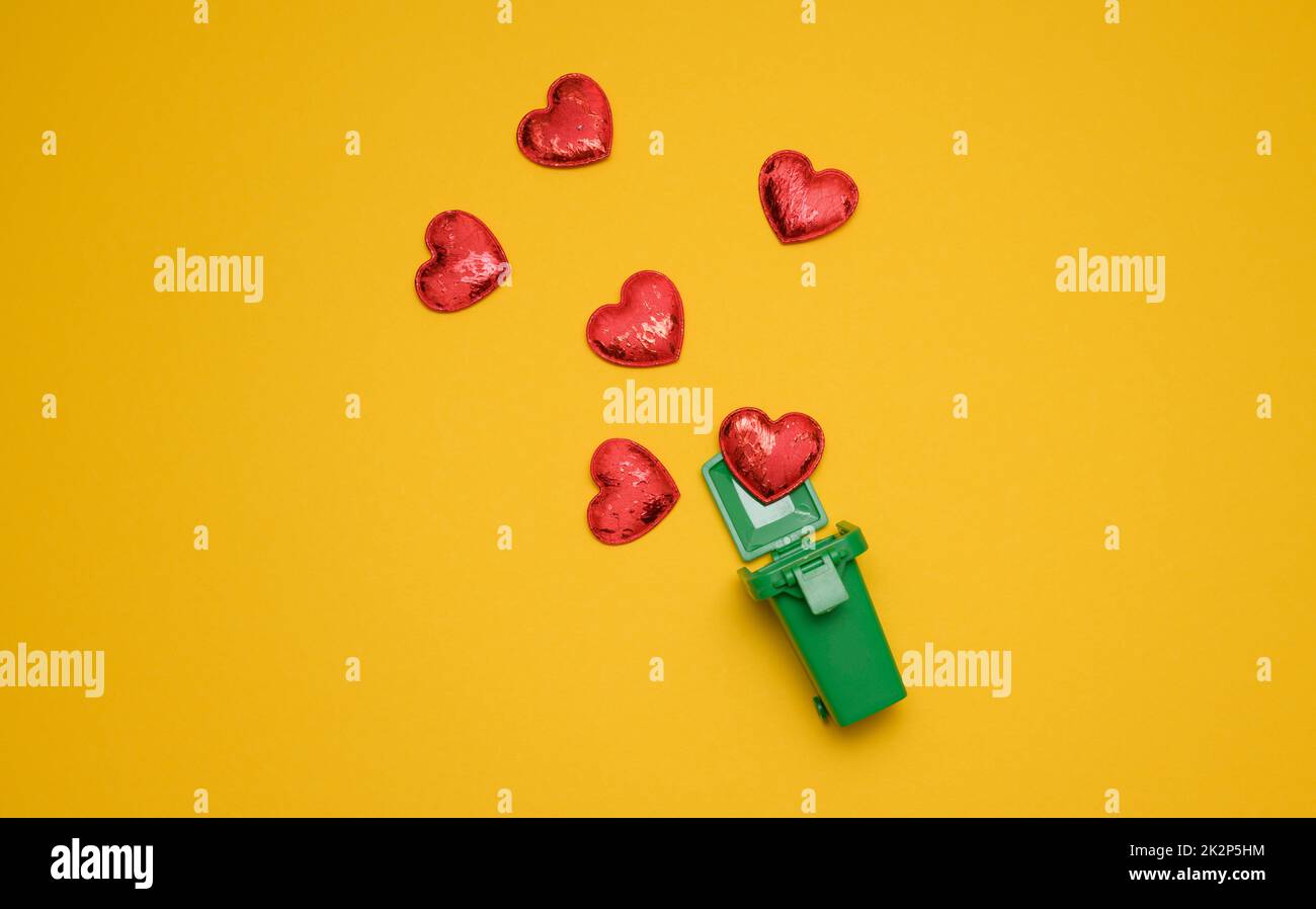 red hearts and a miniature plastic box for collecting garbage on a yellow background Stock Photo