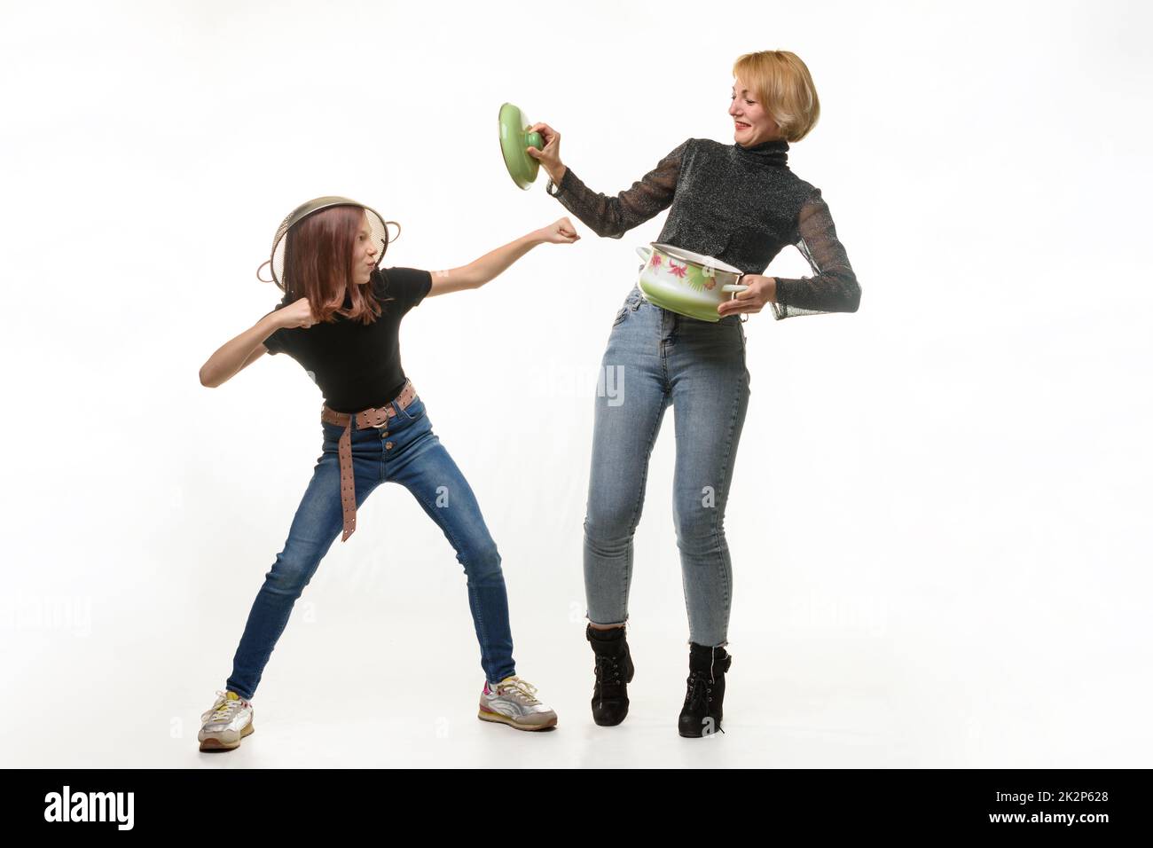 Mom and daughter have fun using kitchen utensils, the girl attacks, mom defends herself with a pot lid Stock Photo