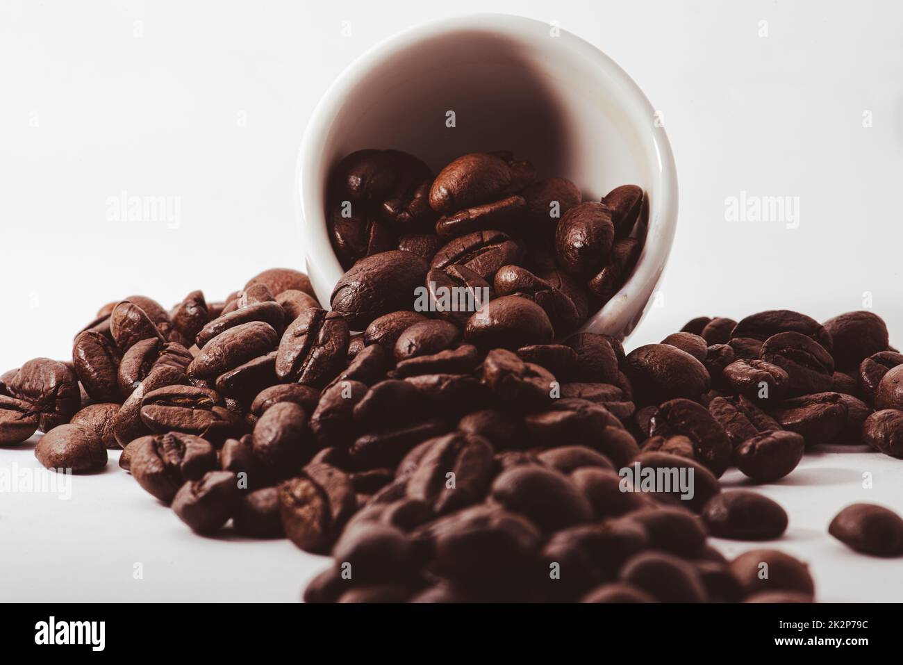 A closeup of brown coffee beans falling out of a cup isolated on a ...