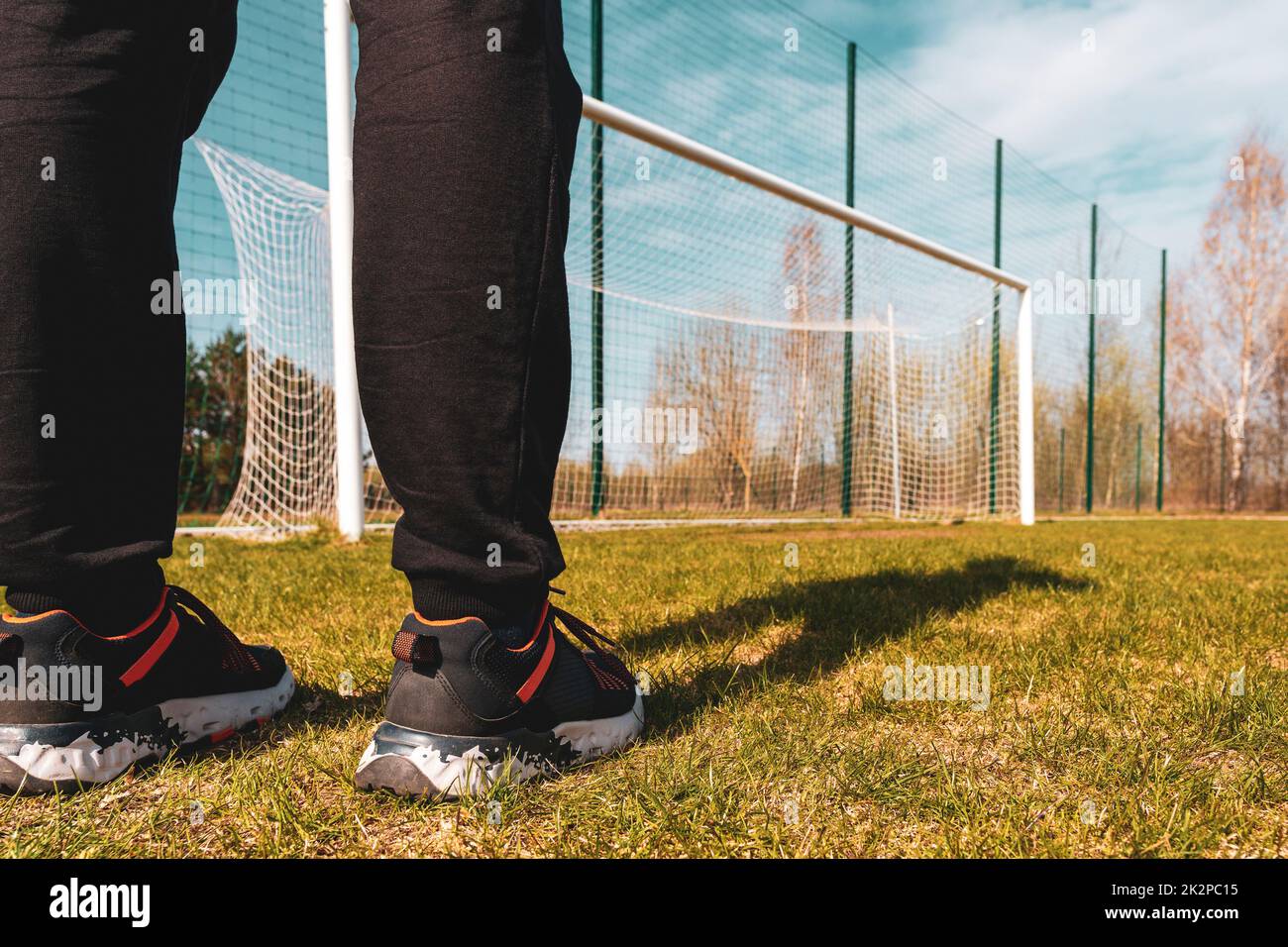 Sportsman  stands in a soccer field against a blue sky and the gate at the stadium Stock Photo