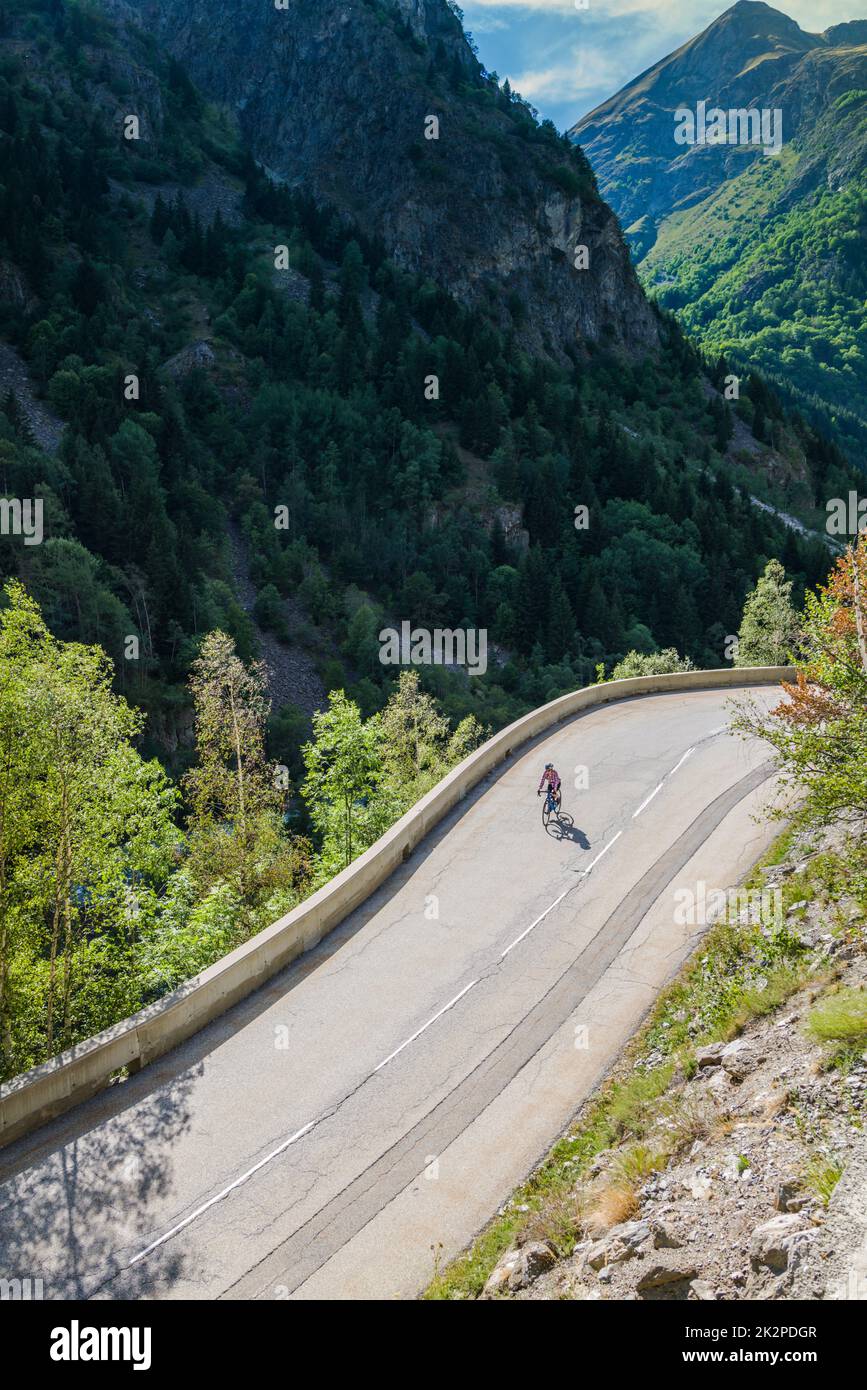 Mature female road cyclist descends a classic alpine road from Saint-Christophe-en-Oisans, French Alps. Stock Photo