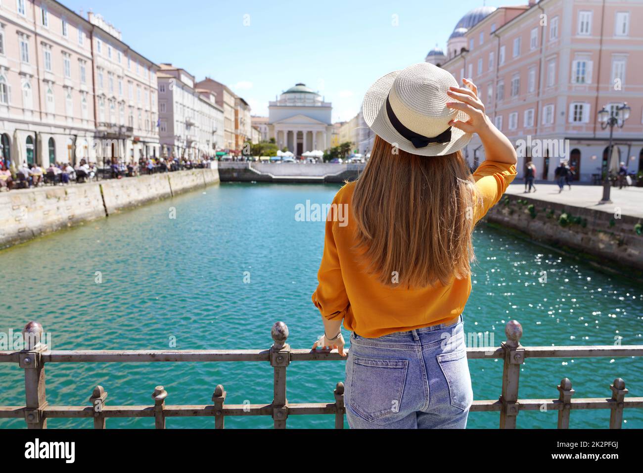 Tourism in Italy. Back view of pretty girl holding hat in Trieste, Italy. Beautiful young woman visiting Europe. Stock Photo