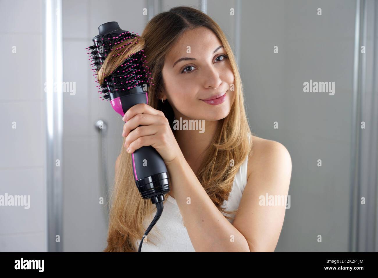 Girl using round brush hair dryer to style hair at the mirror in an