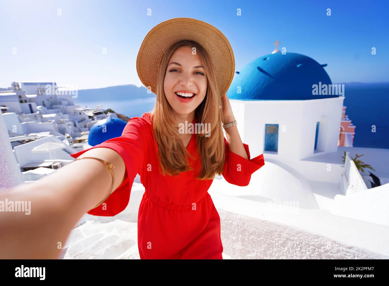 Happy young woman takes selfie photo between Oia famous blue domes churches on Santorini Island. Self portrait of beautiful girl in Santorini, Greece. Stock Photo
