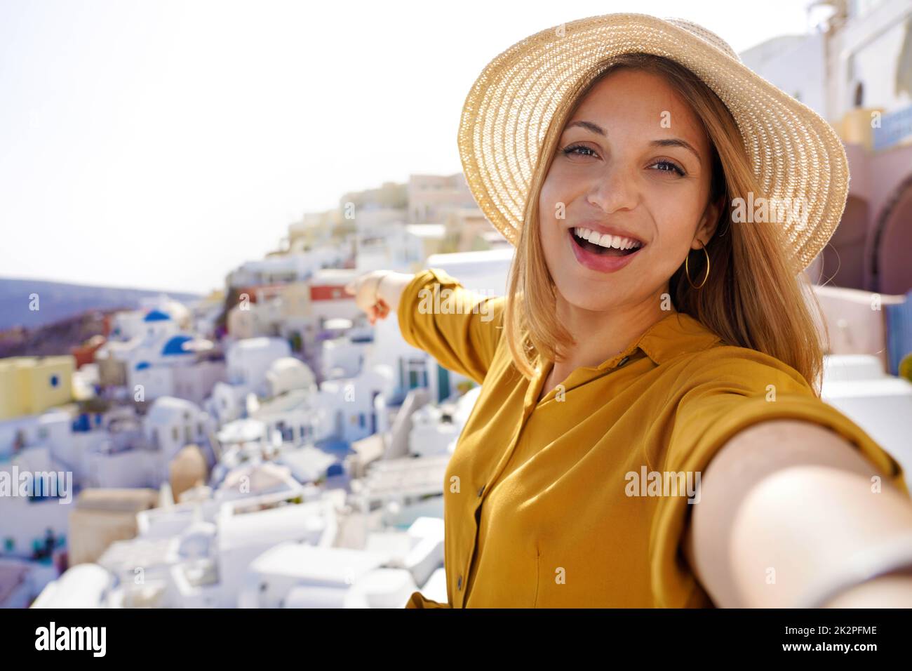 Beautiful young woman taking self portrait showing Oia famous village
