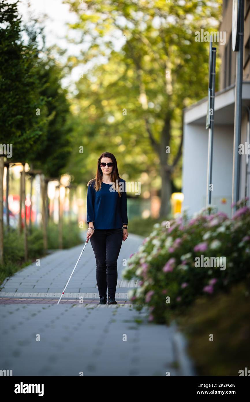 Blind woman walking on city streets, using her white cane to navigate the urban space better and to get to her destination safely Stock Photo