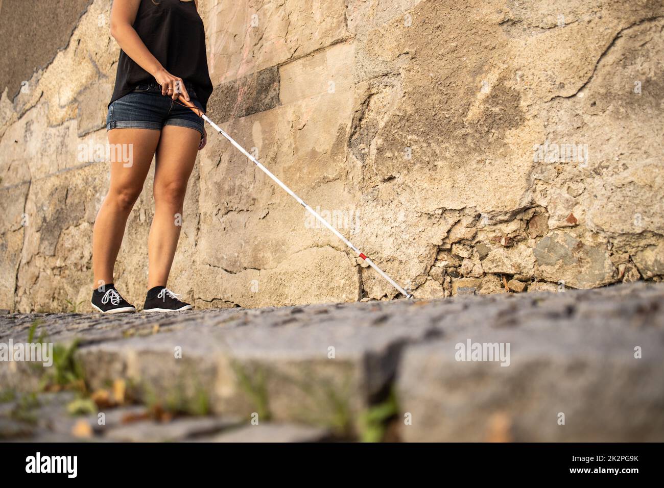 Blind woman walking on city streets, using her white cane to navigate the urban space better and to get to her destination safely Stock Photo