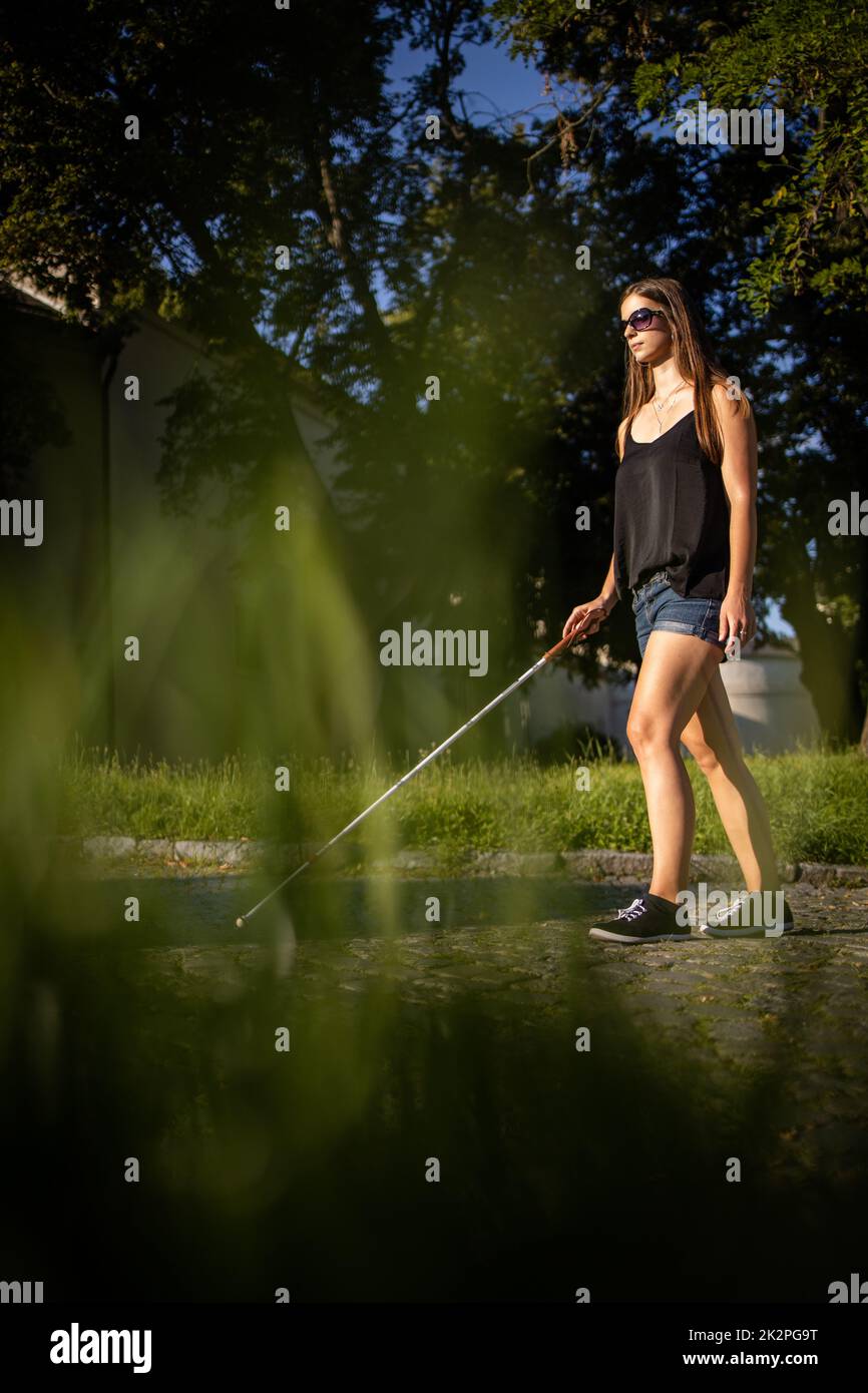 Blind woman walking on city streets, using her white cane to navigate the urban space better and to get to her destination safely Stock Photo