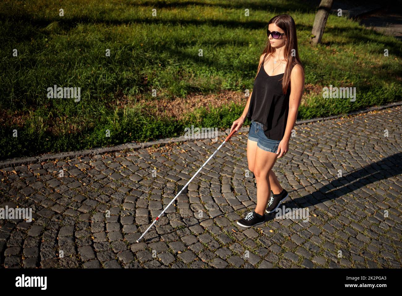 Blind woman walking on city streets, using her white cane to navigate the urban space better and to get to her destination safely Stock Photo