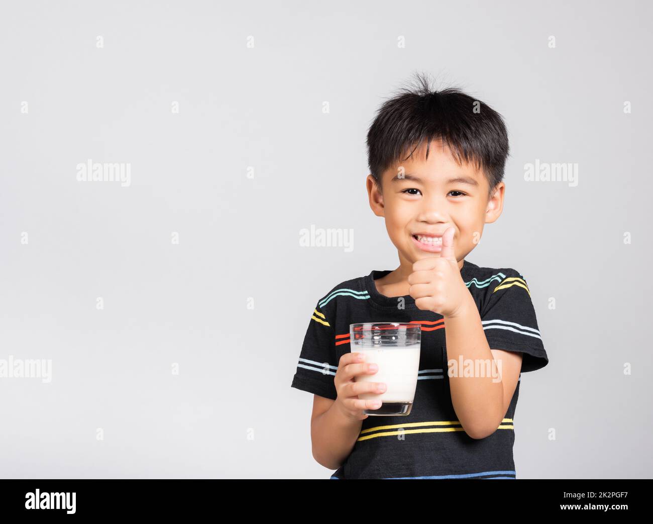 Little kid boy 5-6 years old smile holding milk glass he drinking white milk and show thumb up finger for good sign Stock Photo