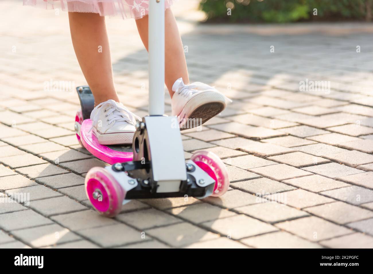 Happy Asian little kid girl wear safe helmet playing pink kick board on road in park outdoors on summer day Stock Photo