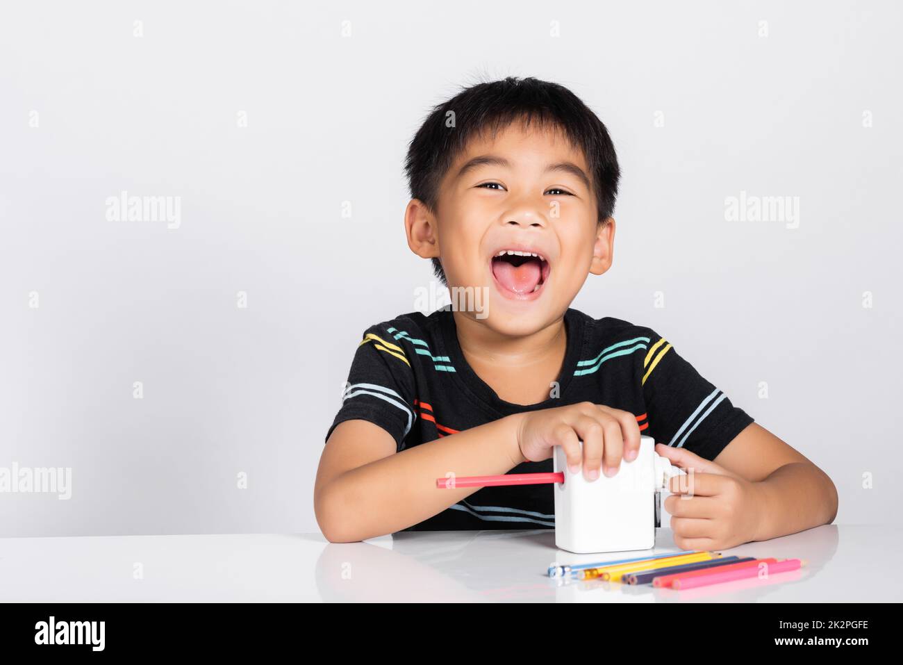 Little cute kid boy 5-6 years old smile using pencil sharpener while doing homework Stock Photo