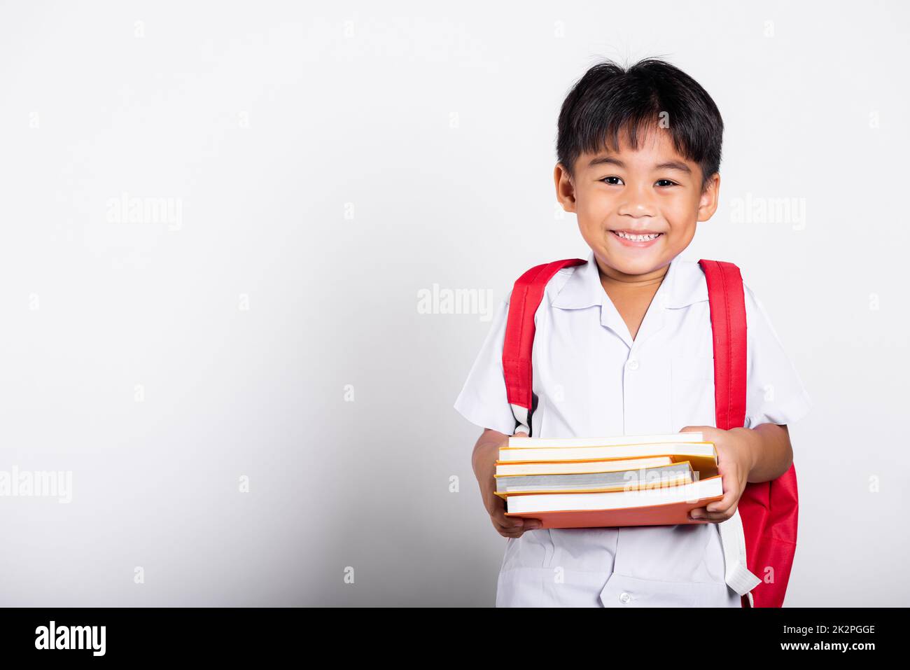Asian adorable toddler smiling happy wearing student thai uniform red pants stand books for study ready for school Stock Photo