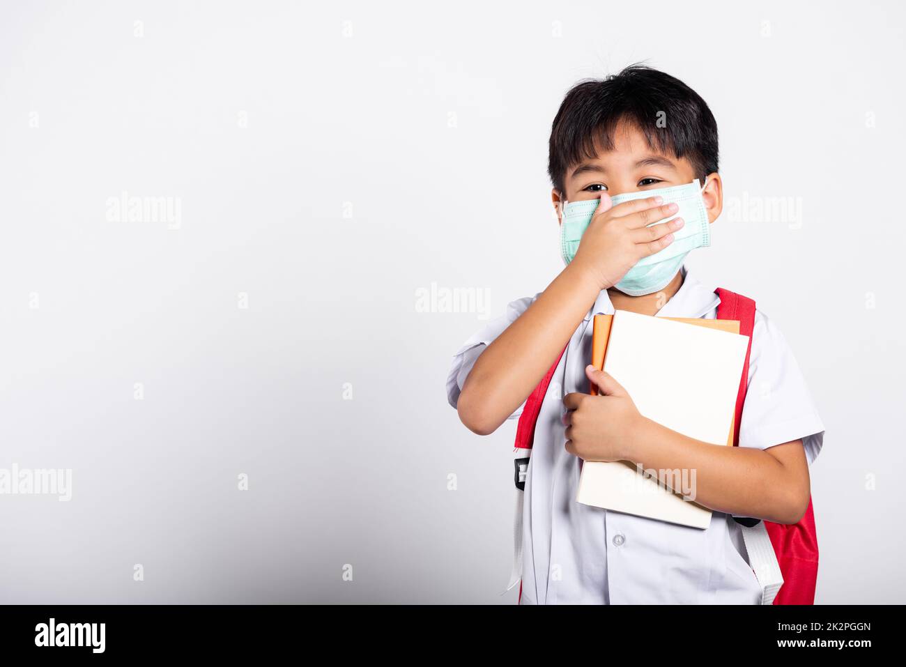 Asian student kid boy wearing student thai uniform and medical protect face mask and hand cover mouth Stock Photo