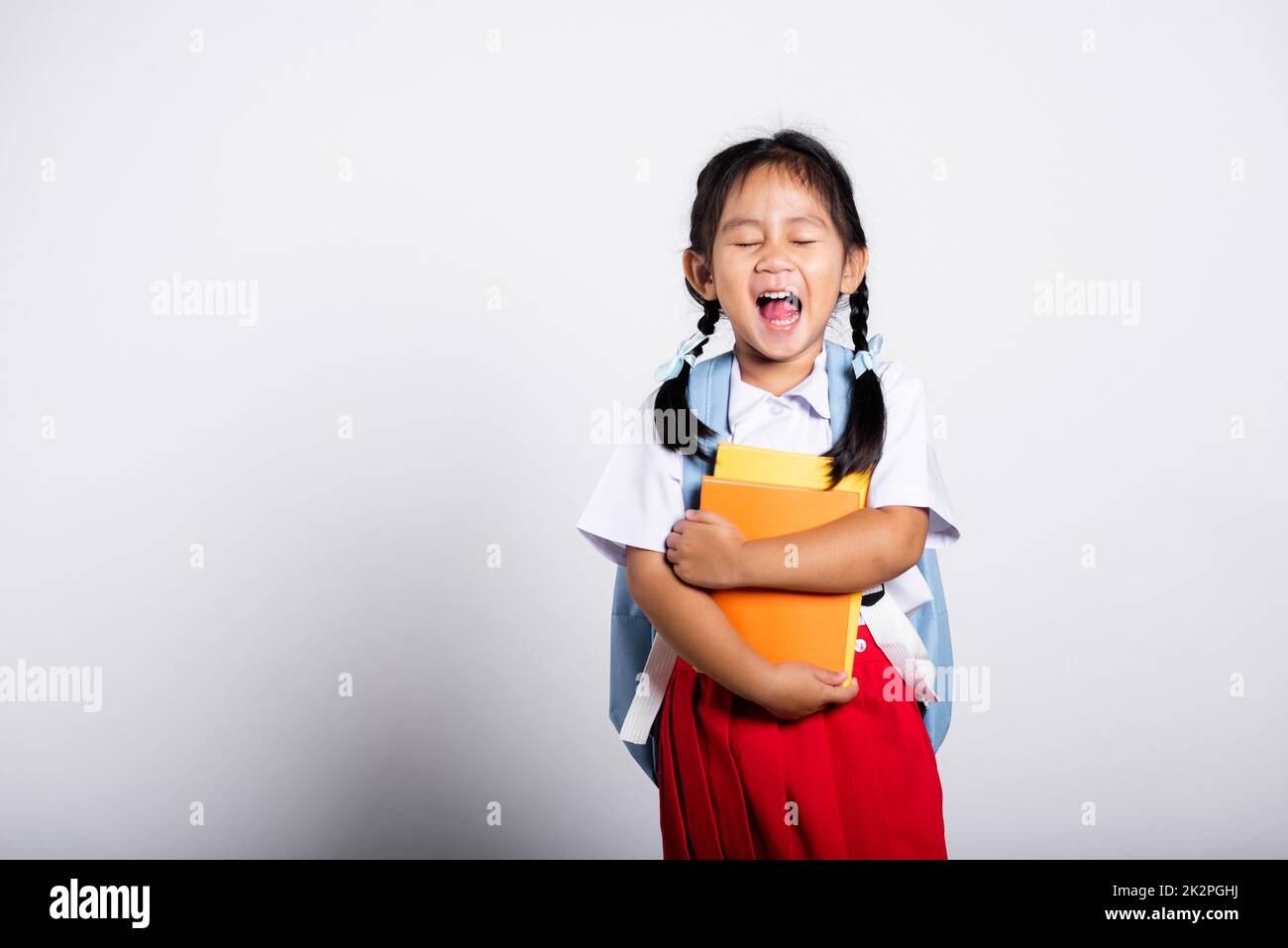 Asian adorable toddler smiling happy wear student thai uniform red skirt stand hold or hugging book Stock Photo