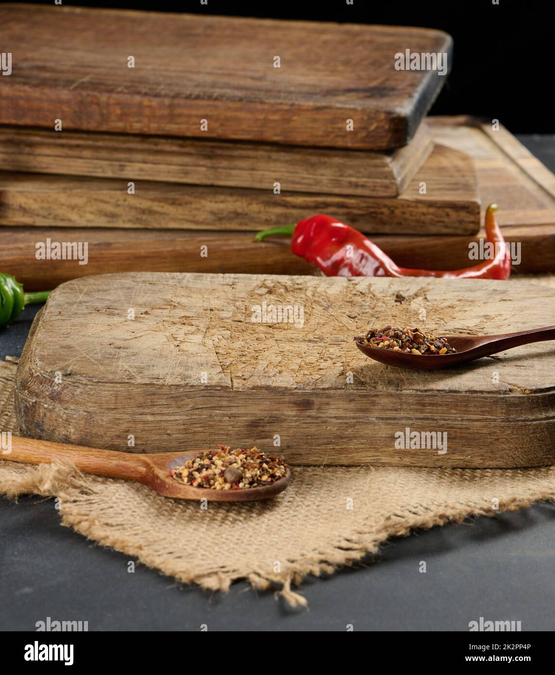 empty kitchen brown wooden cutting board on black table, next to spoons with spice and fresh chili, black background Stock Photo