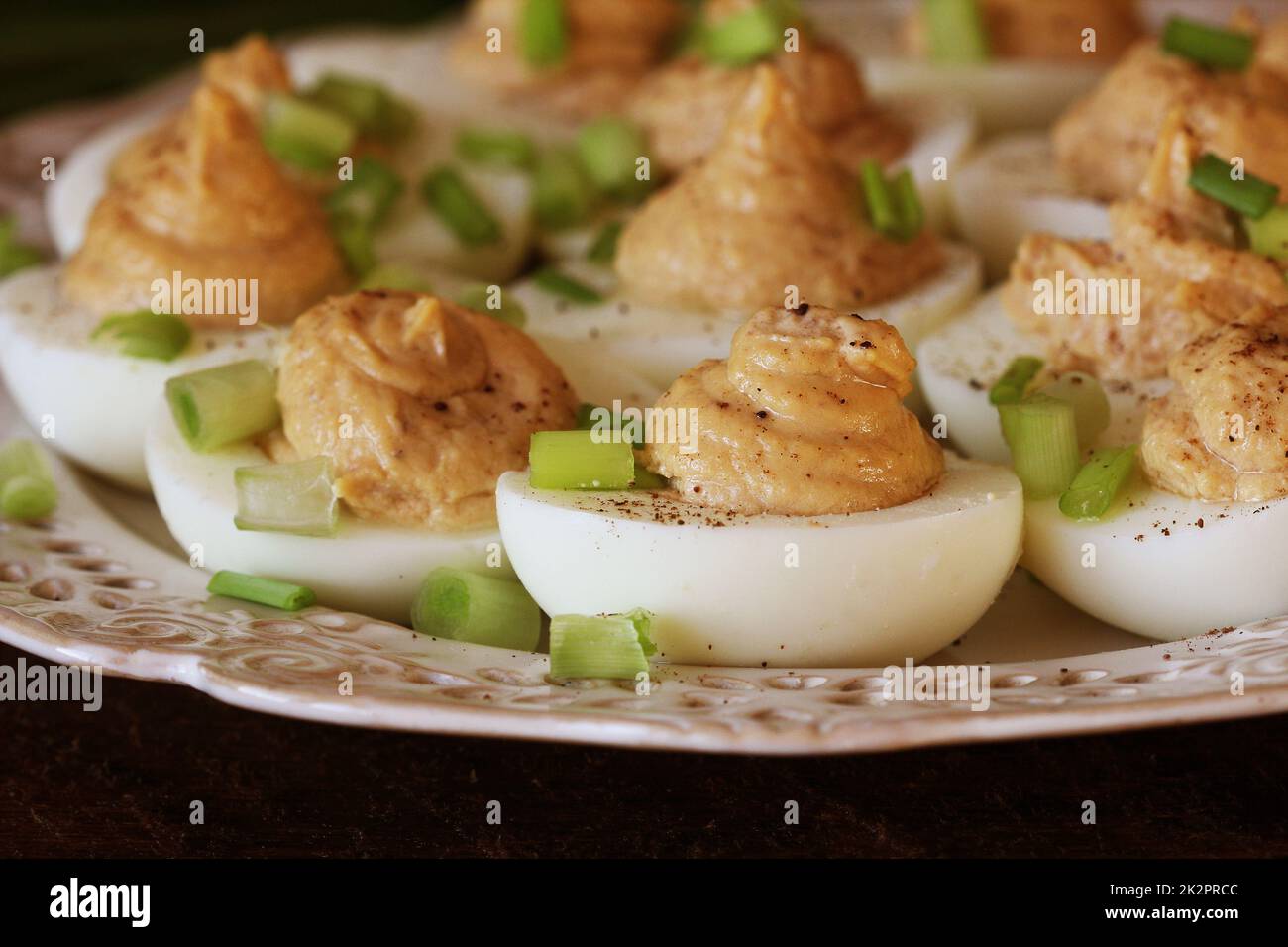 Deviled eggs with cod livers with leek on white plate. Rustic wooden table Stock Photo