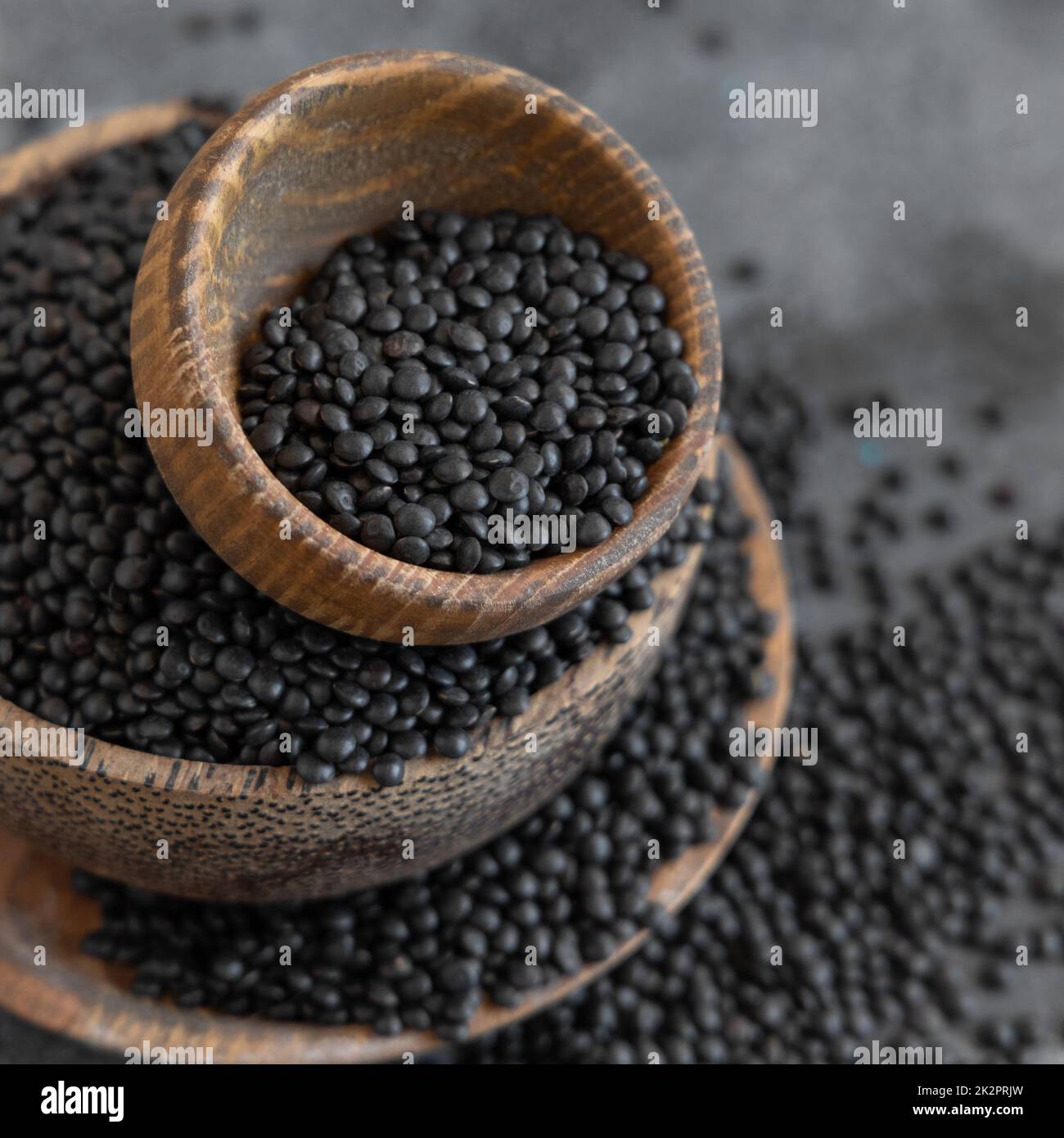 Wooden bowls of dry black lentils beans on grey table close up, protein