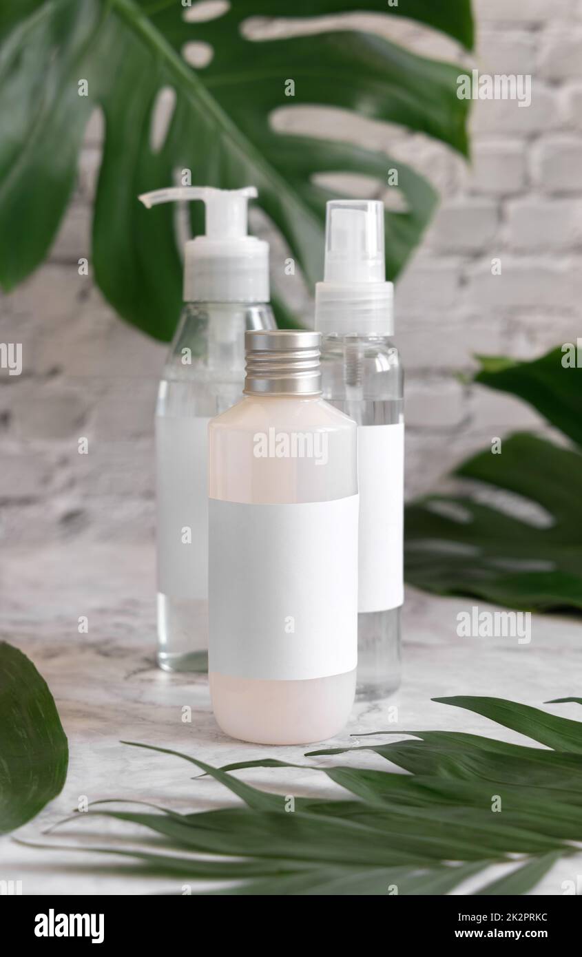 Trasparent cosmetic dispensers and monstera leaves on marble table close up. Brand packaging mockup Stock Photo